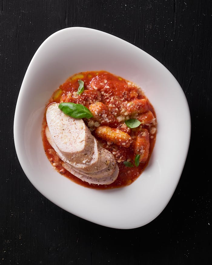 Services Close-up of Italian gnocchi with marinara sauce, cheese, and basil leaves.
