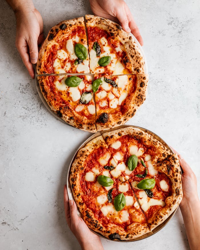 About Delicious Margherita pizzas with basil leaves held by hands on a rustic gray table.