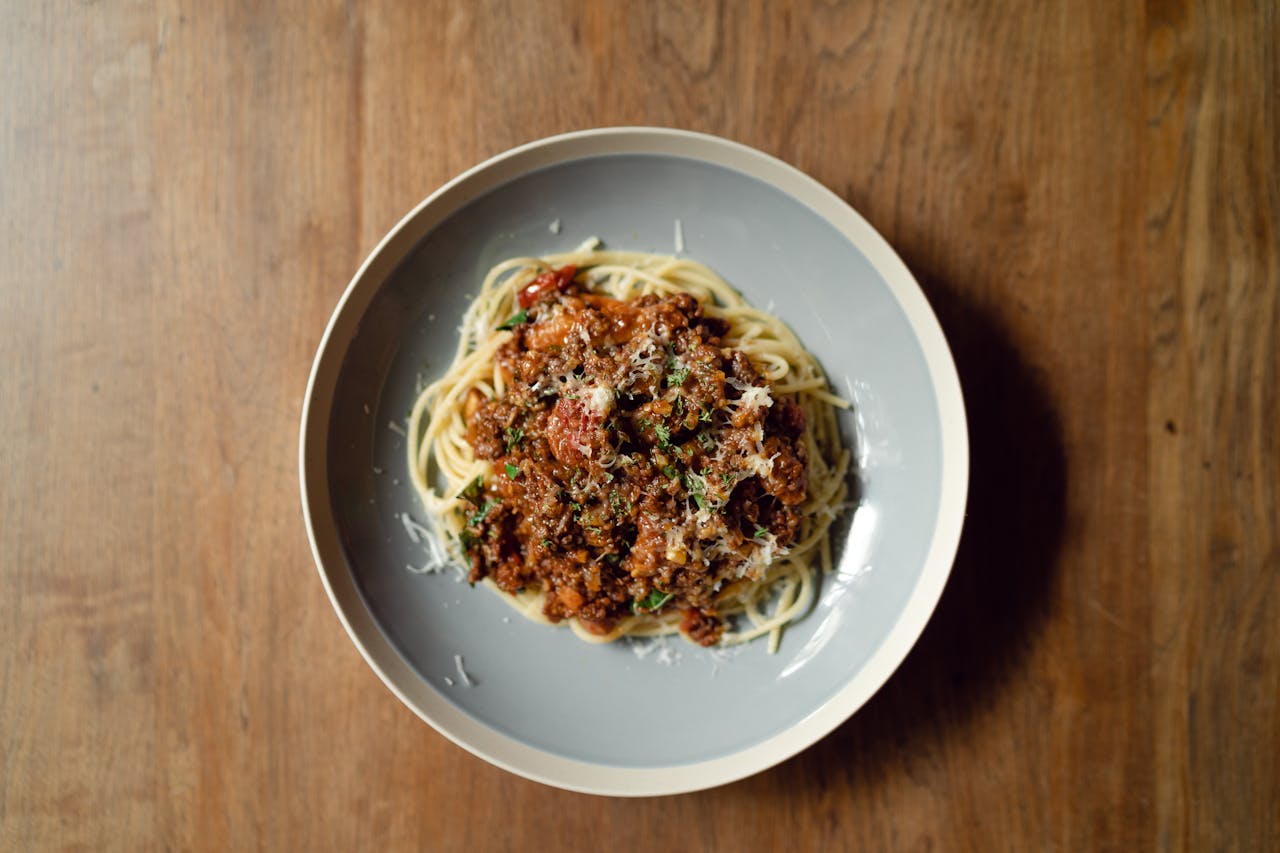 Crafting Captivating Headlines: Your awesome post title goes here Top view of round plate with delicious Italian pasta Bolognaise garnished with grated parmesan cheese placed on wooden table