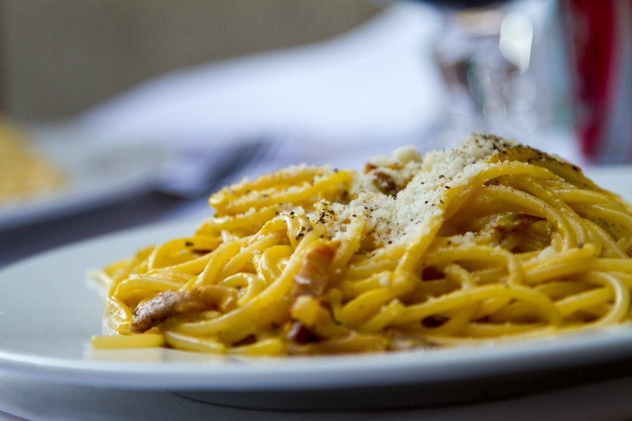 About Close-up of spaghetti carbonara topped with grated Parmesan cheese on a plate, perfect for Italian cuisine lovers.