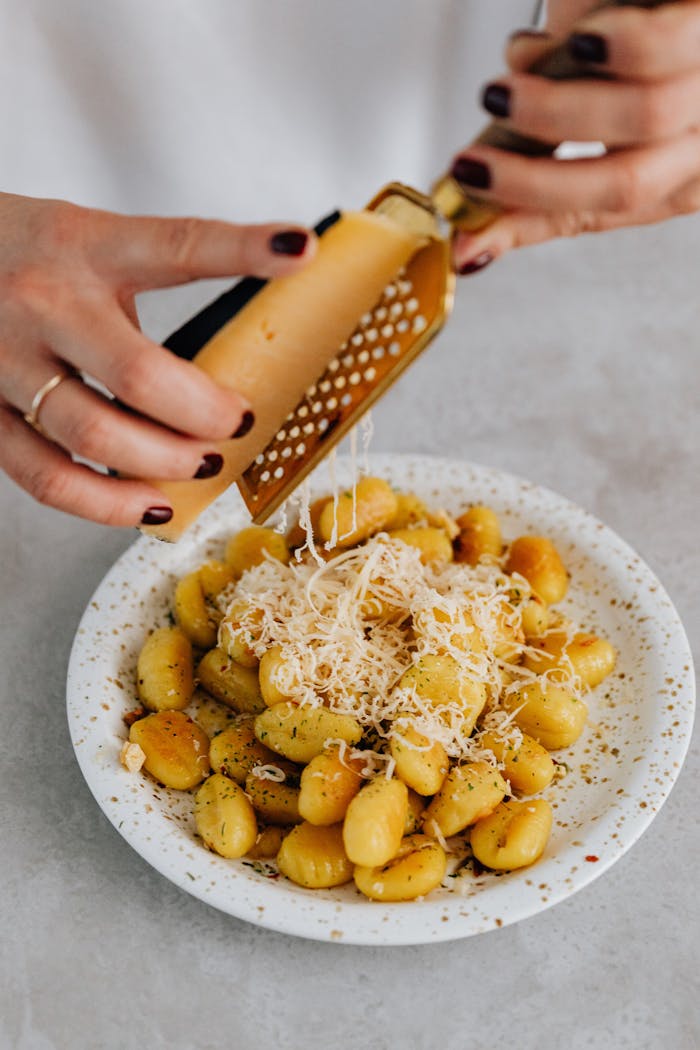 Services A person grates parmesan cheese over a freshly prepared gnocchi dish, Italian cuisine delight.
